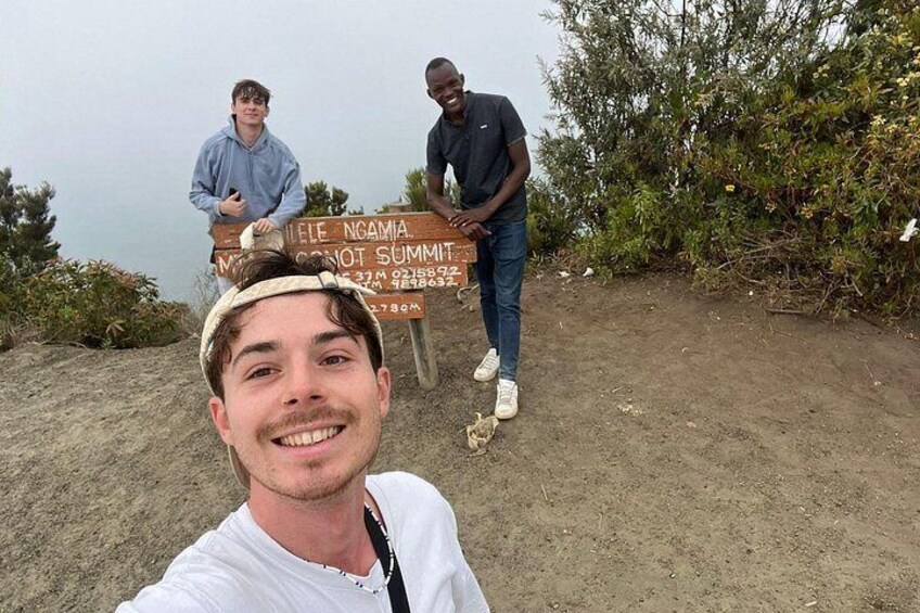A sign with text, a person in a white shirt, and another person in a dark shirt standing near a bush. 2