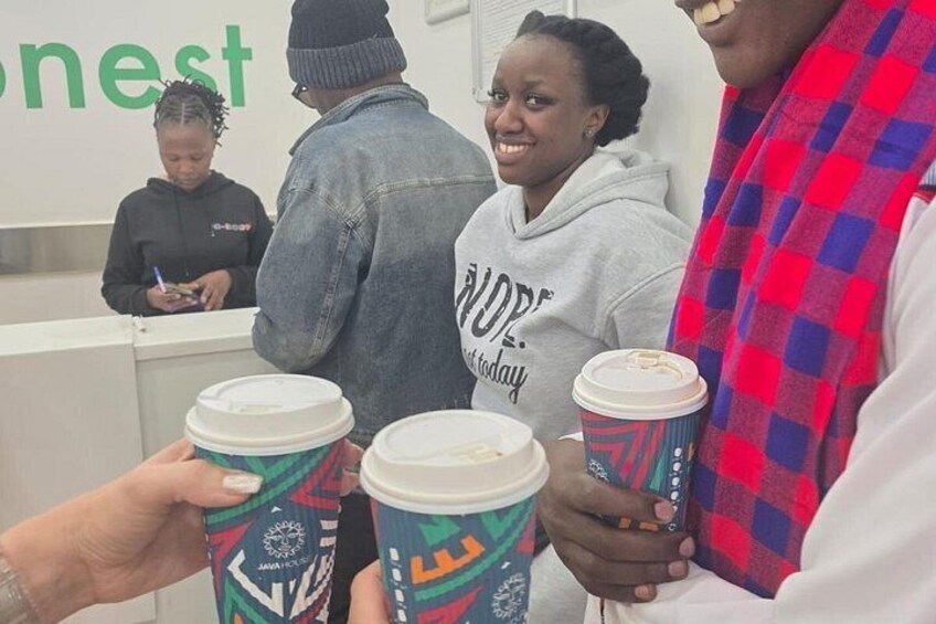 People holding coffee cups with colorful lids, standing in front of a counter with a person behind it. 4