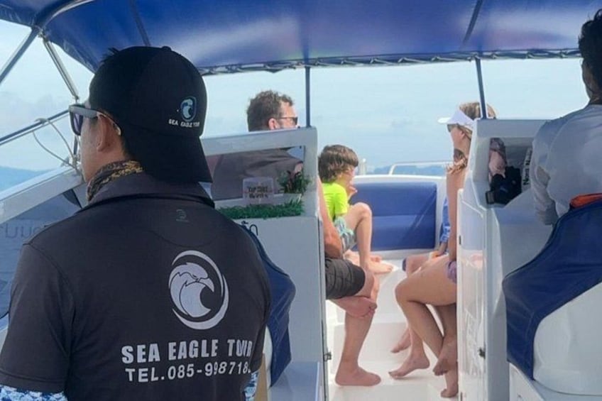 A boat with people on board, a man in a black shirt with a logo, and a child in a green swimsuit. 3