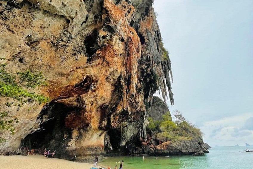 A coastal cliff with a cave entrance, beach, and calm sea. 5