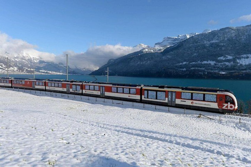 Un tren sobre rieles con suelo cubierto de nieve y montañas al fondo. 2