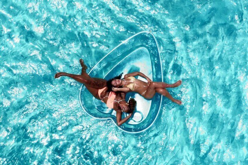 Vue aérienne d’une piscine où l’on voit deux personnes flotter sur un grand flotteur gonflable en forme d’anneau. 3