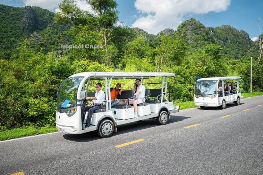 Two white open-top vehicles on a road with lush greenery and mountains in the background. 5