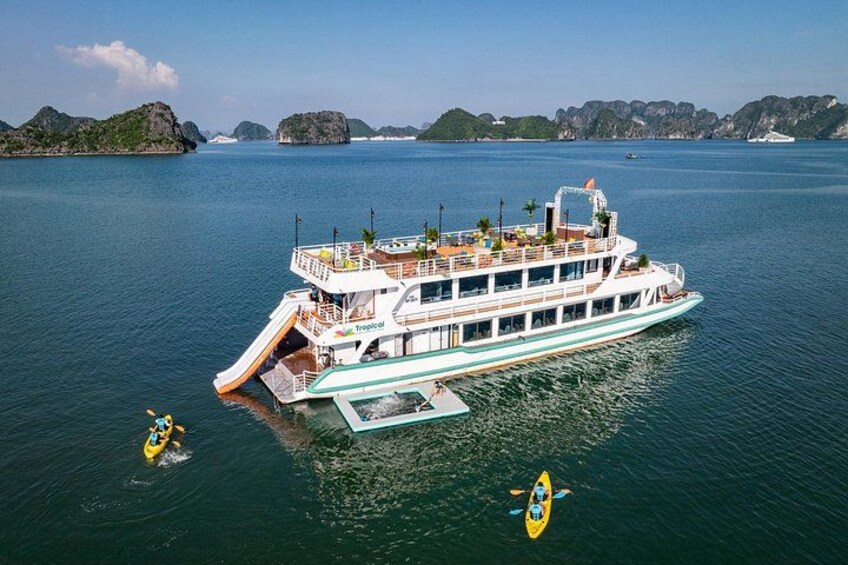 A large white boat with a deck and a slide, surrounded by calm water and distant islands. 1