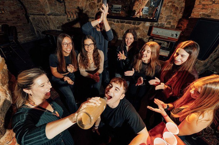 A group of people in a dimly lit room with stone walls, engaged in a social gathering. 2