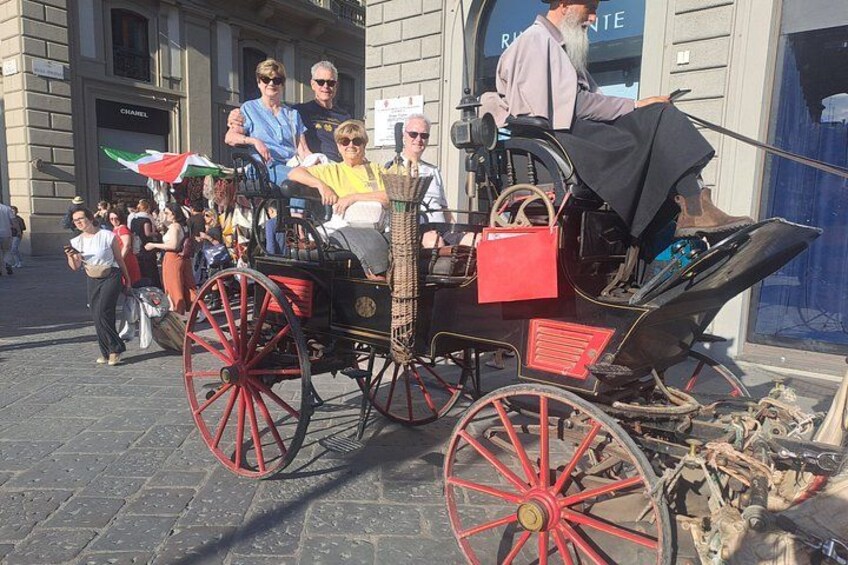A horse-drawn carriage with passengers, a cobblestone street, and a building with a sign that reads 'CHANEL'. 2