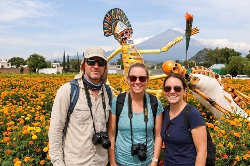 Three people standing in front of a large skeleton sculpture with a mountain in the background. 3