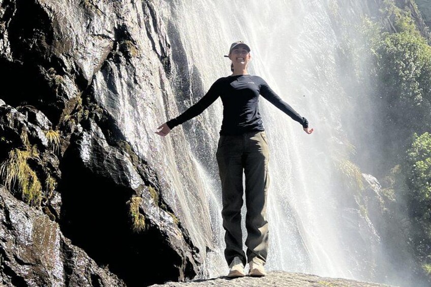Una persona de pie sobre una roca con los brazos extendidos frente a una cascada. 3