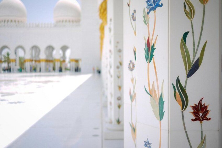 Una mezquita con cúpulas blancas y un patio con un muro floral. 2
