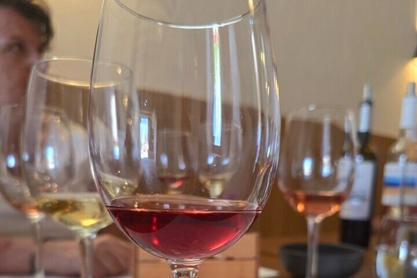 A close-up of a wine glass with red wine, surrounded by other glasses and bottles in a dimly lit setting. 1