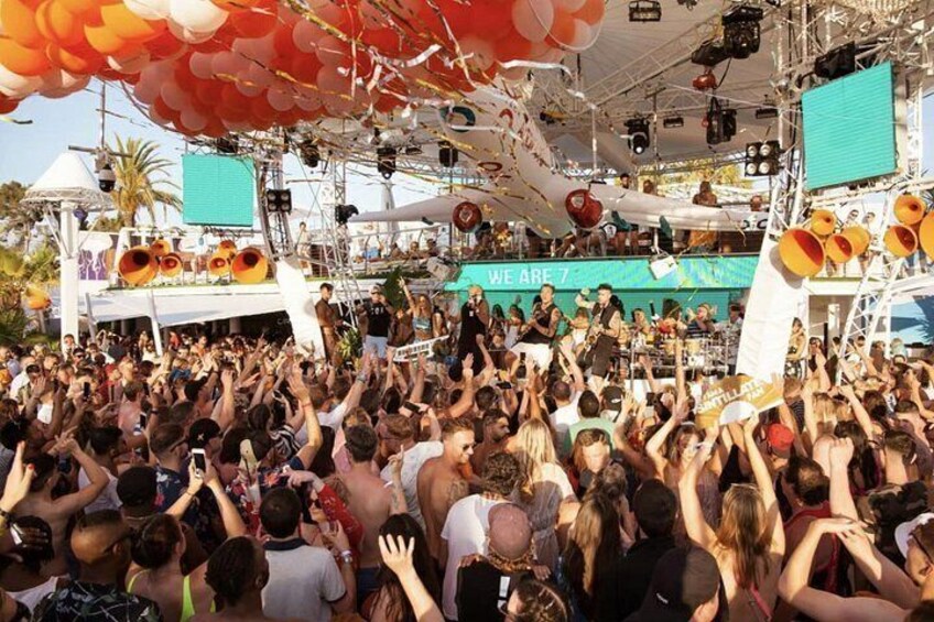 A crowded outdoor event with a stage, speakers, and a banner. 3