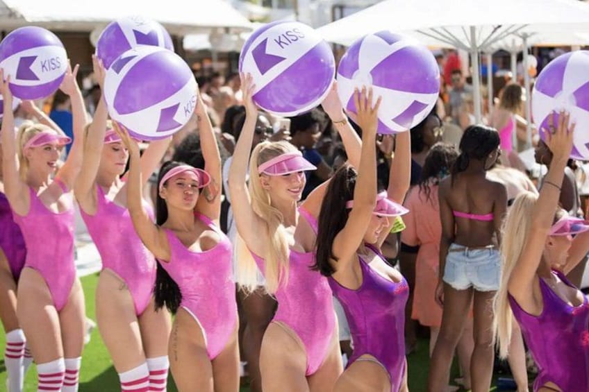 A group of people in pink outfits holding purple volleyballs with the word 'KISS' on them. 4