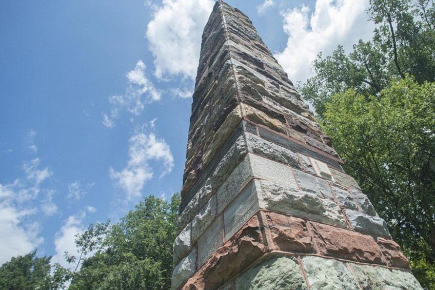 A tall stone monument with layered construction, surrounded by trees and a clear sky. 2
