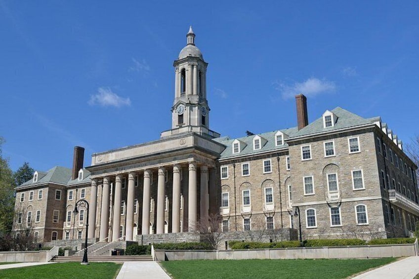 A large, historic building with a prominent clock tower and columns, surrounded by a well-maintained lawn and a clear blue sky. 2