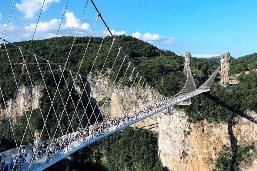 A suspension bridge with people walking across it, surrounded by cliffs and greenery. 1