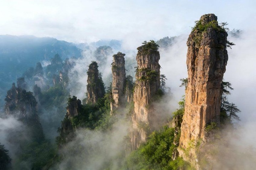 Towering rock formations with dense vegetation, surrounded by misty mountains. 5