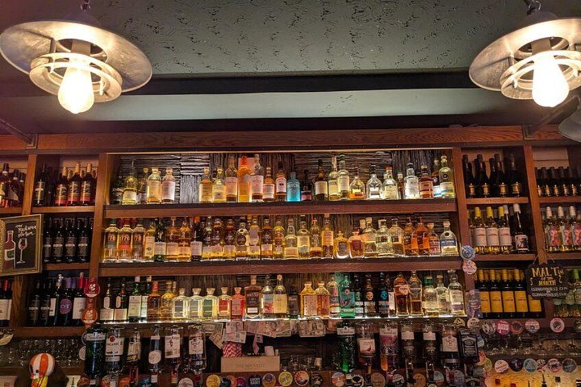 En bar med hylder fyldt med forskellige flasker spiritus. 4