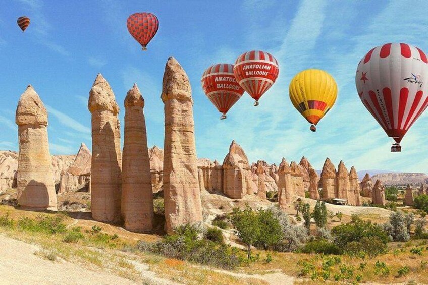 A landscape with tall rock formations and hot air balloons in the sky. 3