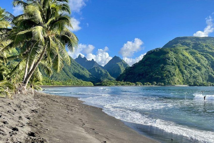 A beach with palm trees, a mountain range, and a person surfing. 1