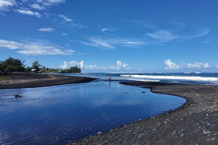 A beach with calm water, a person standing in the water, and waves approaching the shore. 5