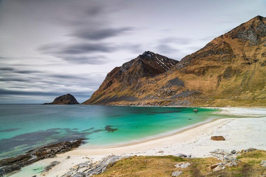 Eine Küstenlandschaft mit Strand, klarem türkisfarbenem Wasser und zerklüfteten Bergen. 4