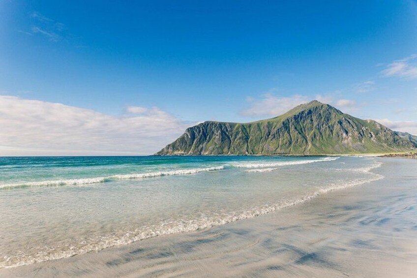 Ein Strand mit klarem türkisblauem Wasser, einem Sandufer und einem Berg im Hintergrund. 2