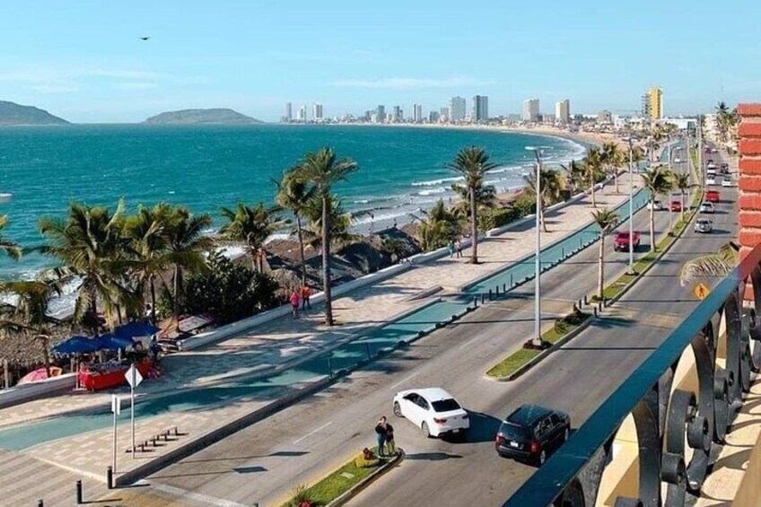 A coastal road with palm trees, a beach, and a city skyline in the background. 4