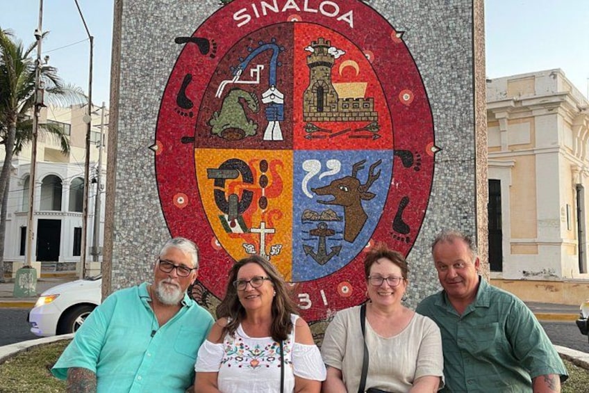 En gruppe mennesker foran et stort emblem med ordet 'SINALOA'. 2