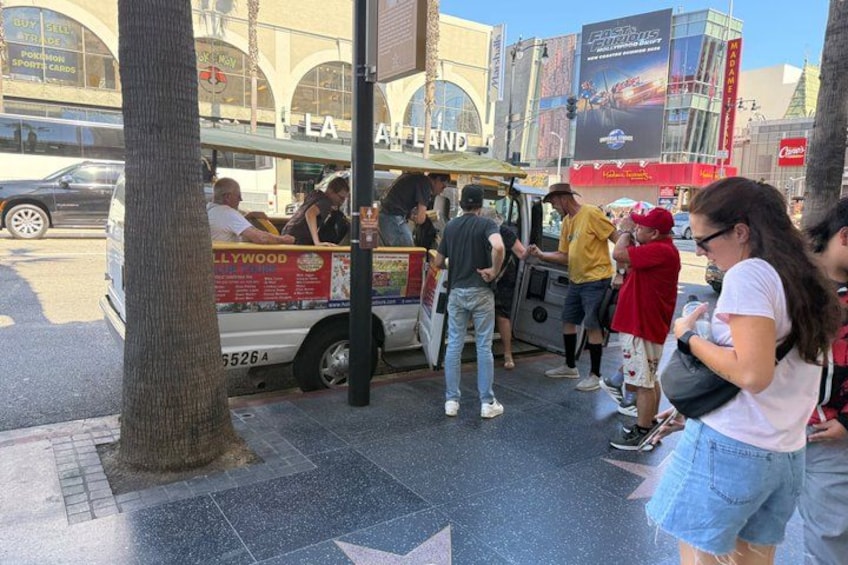 A street food truck with people gathered around it, a tree, and a building with arched windows in the background. 3
