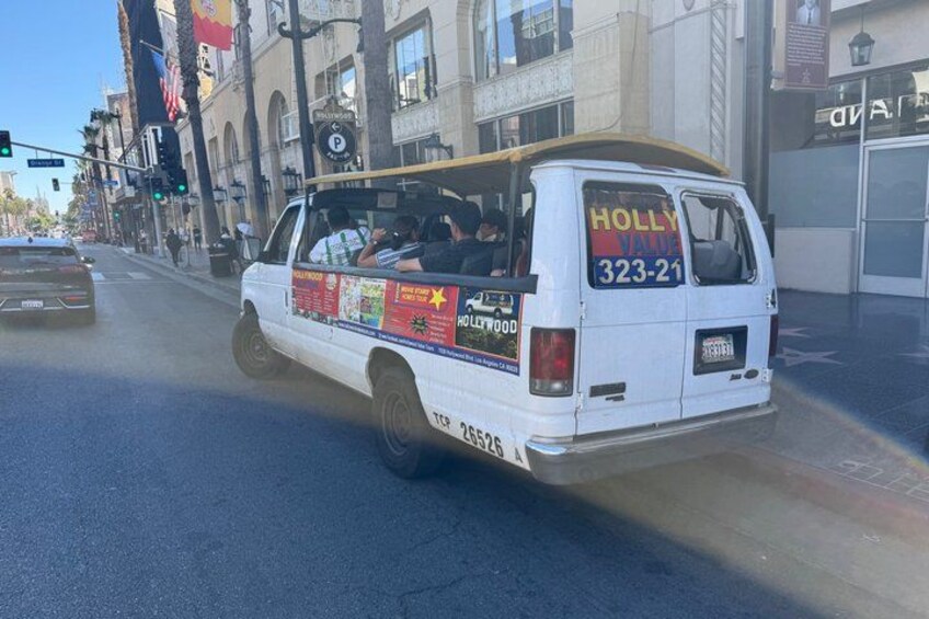 A white van with 'HOLLYWOOD' and '323-21' on the back, driving on a city street. 2