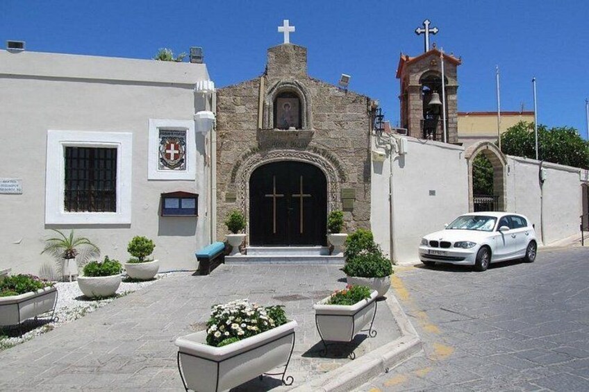 A church with a bell tower, a white car parked in front, and potted plants in the foreground. 3