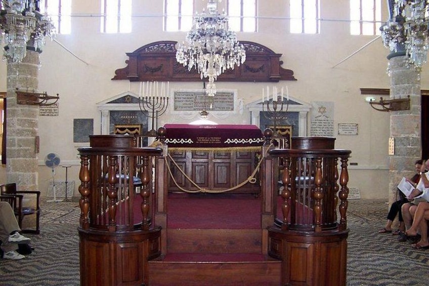 An ornate synagogue interior with a central wooden ark, a chandelier, and a Torah scroll on a stand. 4