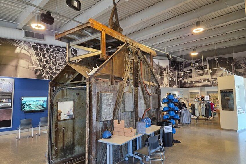 An industrial setting with a large metal structure, a display of blue helmets, and a wall with circular patterns. 2