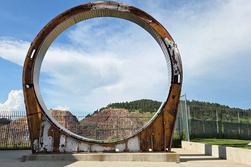 A large circular metal structure with rust, set against a backdrop of a fenced area and distant hills. 3