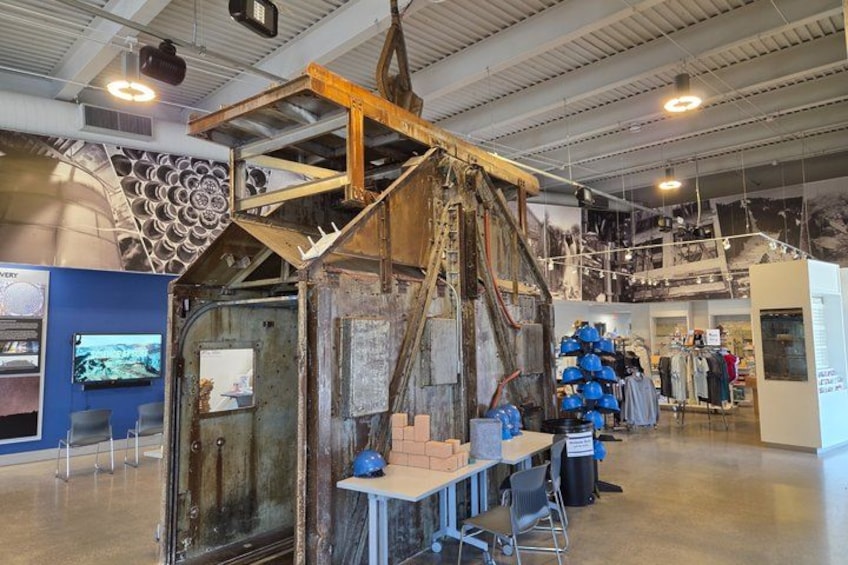 Una obra en construcción con una gran estructura metálica, una exhibición de cascos y un panel informativo azul. 2