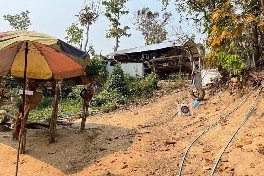A dirt path with a makeshift shelter, a building in the background, and a tree with yellow leaves. 4