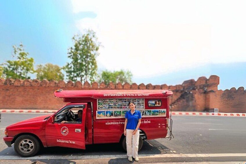 A red food truck parked on a road with a brick wall and trees in the background. 2