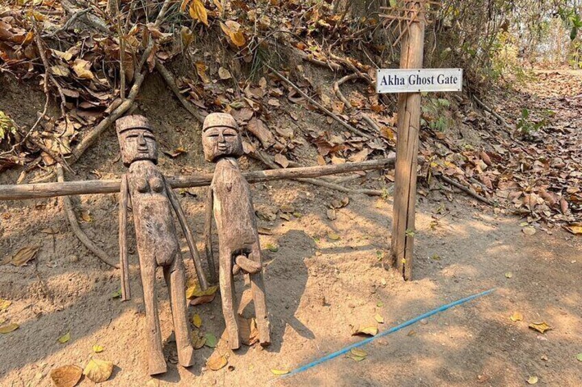 Un letrero de madera que dice "Akha Ghost Gate" con dos estatuas de madera al fondo. 3