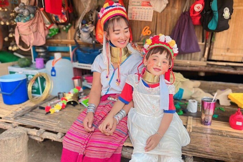 Two people in traditional attire sitting on a wooden bench with various items in the background. 4