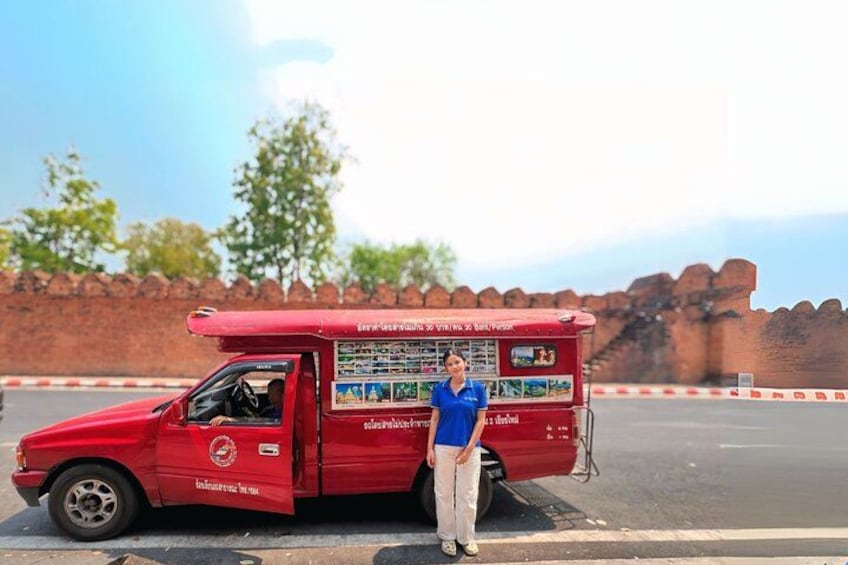 A red food truck parked on a road with a brick wall and trees in the background. 2