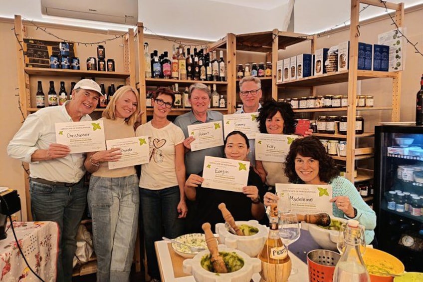 Un grupo de personas sosteniendo certificados en una habitación con estantes llenos de botellas y una mesa con comida. 2