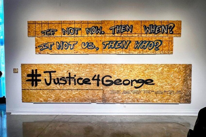 Una pared con dos paneles grandes. El panel superior tiene el texto '¿SI NO AHORA, CUÁNDO? ¿SI NO NOSOTROS, QUÉNES?' El panel inferior tiene el texto '#Justice4George'. 5