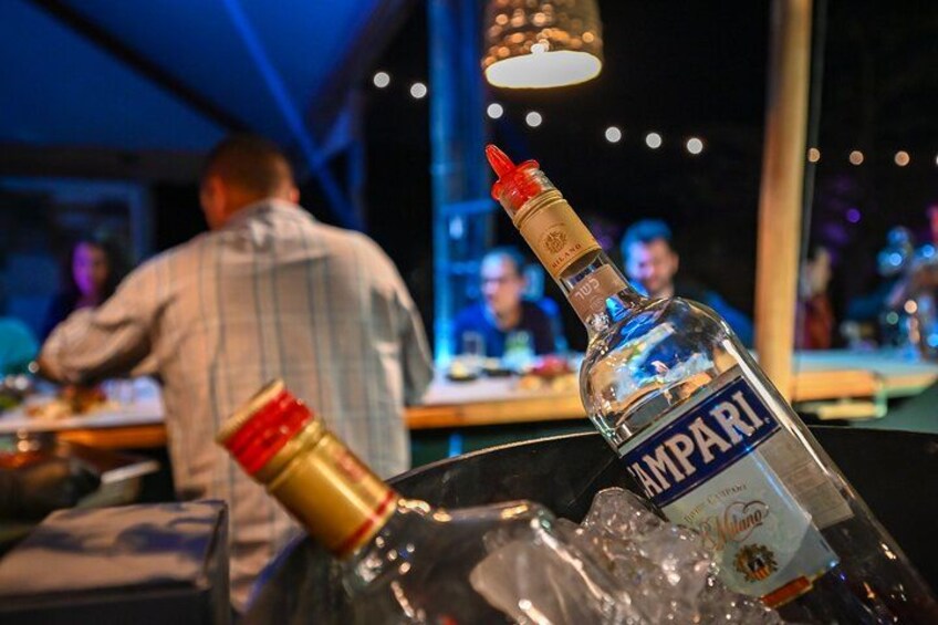 Eine Flasche Campari-Likör in einem Glasgefäß mit Eiswürfeln auf einer Bartheke in einer schummrigen Bar. 2