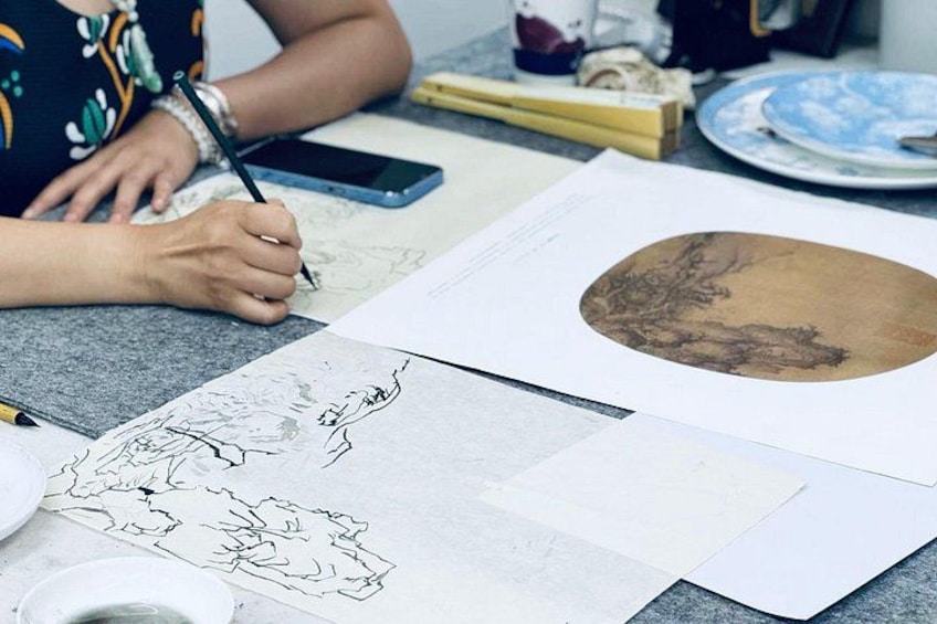 A person drawing on paper with a pencil, surrounded by art supplies and a smartphone. 1