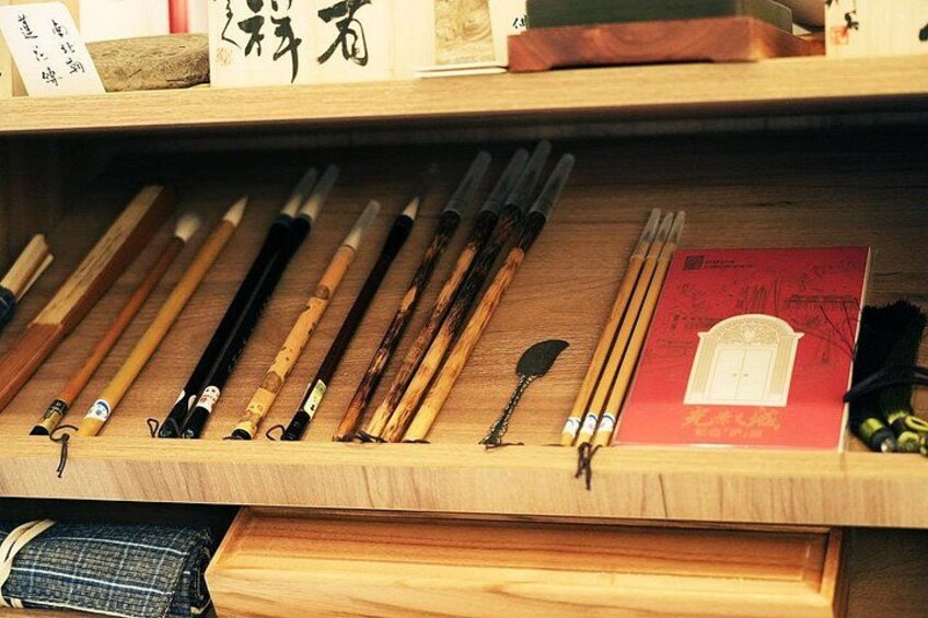 A wooden display case with traditional calligraphy brushes and a red book. 4