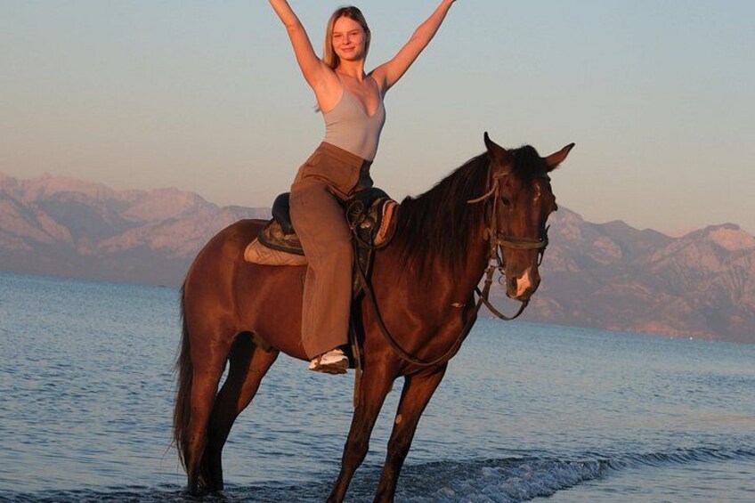 En person rider hest på en strand med bjerge i baggrunden. 4