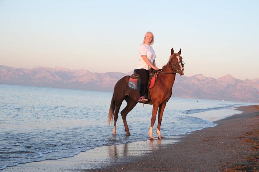 En person rider på en hest ved en strand med bjerge i baggrunden. 3