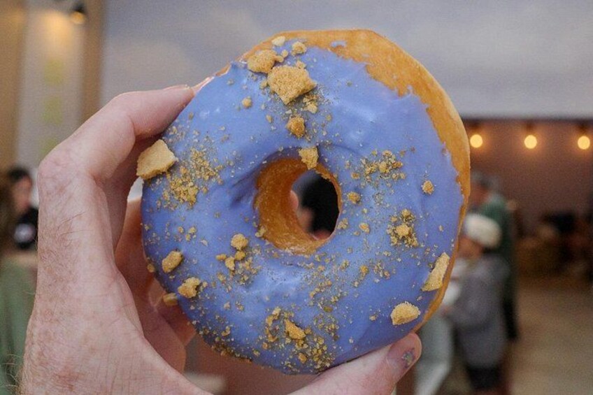 Een hand die een blauw geglazuurde donut met kruimels vasthoudt. 2