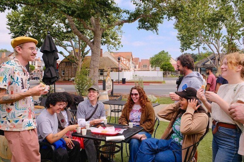 A group of people sitting at an outdoor table, engaged in conversation and enjoying food. 2