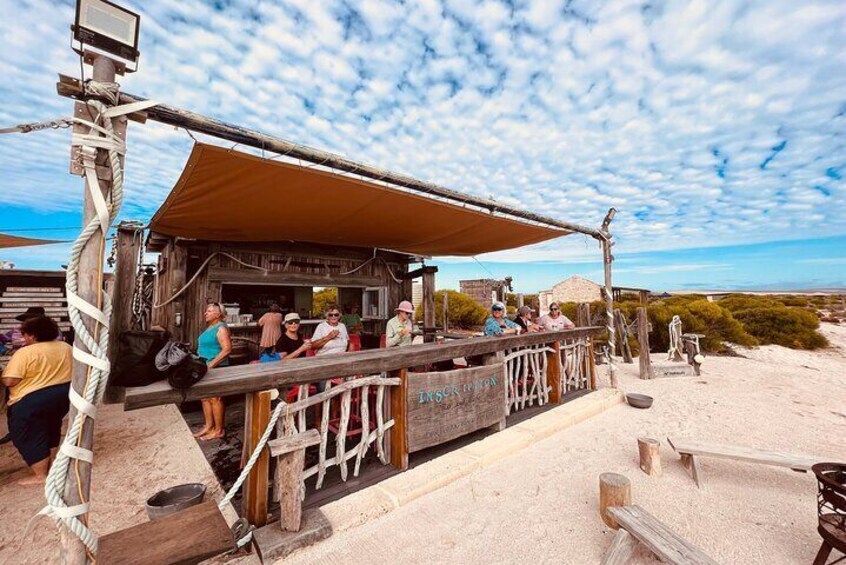 A wooden structure with a roof, surrounded by a sandy area with sparse vegetation. 2